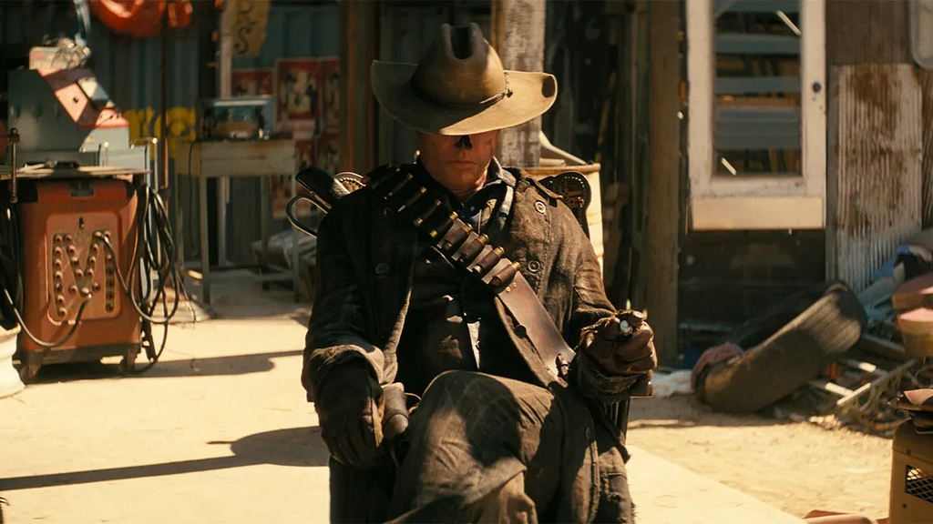 A post-apocalyptic cowboy sitting on a chair in the open